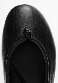Zwarte lederen ballerinas met een afgeronde neus en een klein geknoopt strikdetail bovenop, gezien van bovenaf.