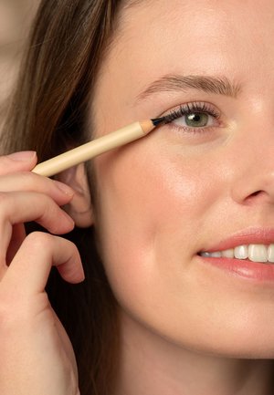 Black eyeliner pencil with a wooden beige casing, applied to the upper eyelid. Skin appears smooth and natural, with soft lighting.