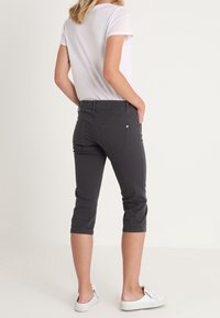 Pantalones capri de algodón grises con un diseño ajustado, de tiro medio, que cuentan con bolsillos traseros y dobladillos acampanados, combinados con una camisa blanca de manga corta.