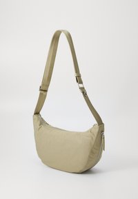 Borsa a spalla beige realizzata in tessuto morbido, con un design arrotondato, tracolla regolabile e chiusura superiore con cerniera che presenta dettagli in metallo argentato.