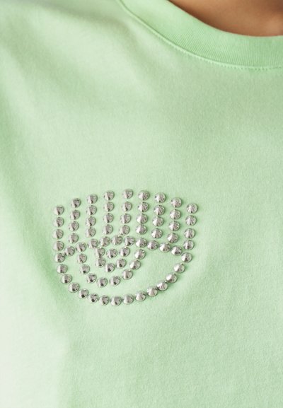 Light green cotton t-shirt featuring a silver rhinestone hand graphic, with smooth texture and circular embellishments outlining the design.