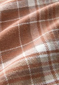 Woven textile featuring a plaid pattern in warm shades of peach and brown, with white accents. Soft texture and subtle herringbone detail.