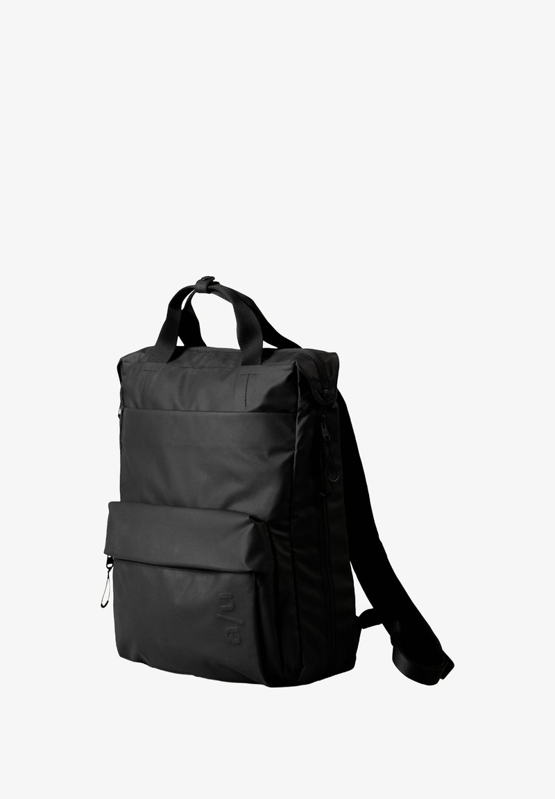 Zaino nero con forma rettangolare, tessuto resistente, maniglie superiori, una tasca anteriore con zipper e spallacci regolabili.