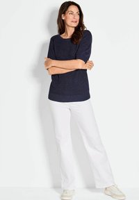 Maglione a maniche corte navy in maglia con scollatura tonda, abbinato a pantaloni bianchi a gamba larga e sneakers di colore chiaro. Texture liscia, vestibilità rilassata.