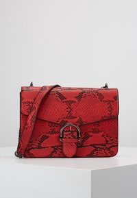 Punainen käärmeennahkakuvioinen käsilaukku, jossa on jämäkkä muoto, läpällä suljettava kansi ja pyöreä metallikoriste. Mukana säädettävä olkahihna.