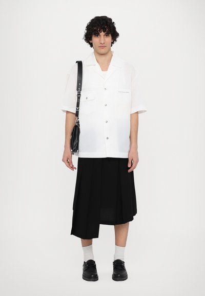 Kurzärmliges weißes Hemd mit zwei Brusttaschen, schwarzer plissierter Rock, schwarze Schuhe und eine schwarze Umhängetasche. Einfarbig, glatte Textur.