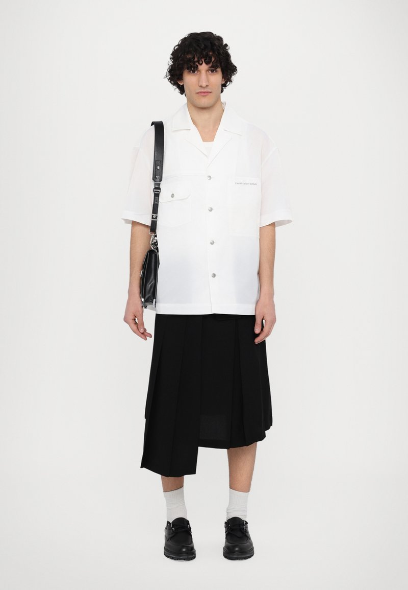 Kurzärmliges weißes Hemd mit zwei Brusttaschen, schwarzer plissierter Rock, schwarze Schuhe und eine schwarze Umhängetasche. Einfarbig, glatte Textur.
