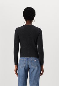 Pull gris foncé côtelé à manches longues et col rond, associé à un jean bleu clair avec un patch logo sur la poche arrière.