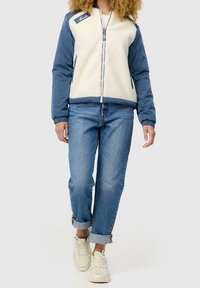 Veste zippée en polaire et nylon de couleur crème et bleue, avec col montant, poignets élastiques et logo brodé sur la poitrine.