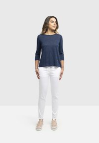 Maglietta a maniche lunghe blu navy con un motivo testurizzato, abbinata a pantaloni bianchi slim-fit e sneaker beige chiaro.