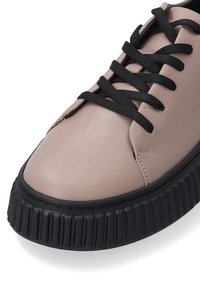 Licht beige leren sneaker met zwarte veters, met een stevige zwarte ribbelzool en een gladde bovenkant.