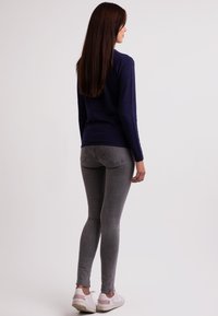 Námořnický pletený svetr v kombinaci se šedými skinny džíny. Obuv tvoří bílé tenisky s jemně růžovými akcenty. Vlasy jsou dlouhé a hnědé.