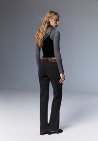 Musta leveälahkeinen farkut ruskealla vyöllä, yhdistettynä tiukkaan mustaan toppiin ja harmaisiin ribattu pitkähihaisiin, nähtynä takaa.