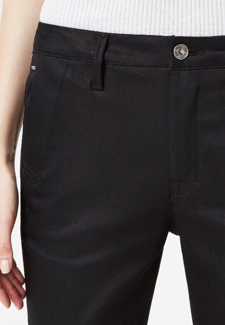 Pantaloni neri in tessuto liscio, con vita classica e chiusura a bottone, tasche laterali e dettagli di cucitura sottili.
