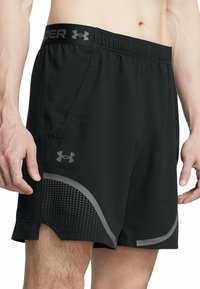 Juodi sportiniai šortai su elastinga juosta, su pilku "Under Armour" logotipu, lenktomis šoninėmis siūlėmis ir dėmėtu raštu.