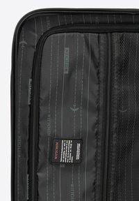 Interno di una valigia da viaggio nera con tessuto liscio, un compartimento con zip e un'etichetta di marca. Rivestimento testurizzato con sottili motivi di aerei.