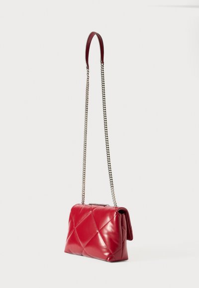 Κόκκινη καπιτονέ δερμάτινη τσάντα ώμου με μακρύ ασημένιο αλυσίδα και δερμάτινη επένδυση ώμου, εκτεθειμένη σε λευκό φόντο.