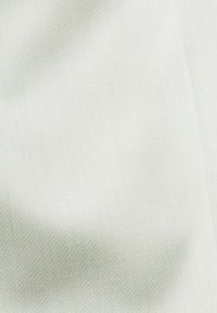 Gros plan sur un tissu blanc texturé avec des plis doux créant des ombres et des reflets subtils.