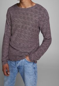 Pull texturé de couleur prune avec un col large et des manches longues, associé à un jean bleu clair. Présente une coupe décontractée et un motif tricoté.