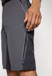 Shorts de sport gris avec une finition texturée, dotés d'une poche zippée sur le côté et de détails de couture visibles.