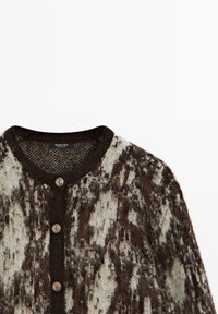 Cardigan en laine marron et beige à motif, col rond et trois boutons métalliques décoratifs sur le devant.