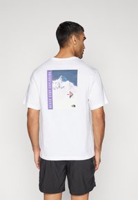 Camiseta de algodón blanca de manga corta, con un gráfico de montaña y la frase "NUNCA DEJES DE EXPLORAR" en púrpura en la parte posterior.