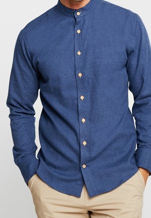 Camisa de botón azul oscuro con cuello mao, presenta botones de madera y mangas largas. La tela parece suave y texturada.