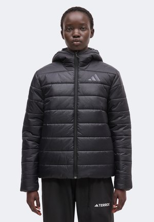 Person trägt eine schwarze gesteppte Kapuzenjacke mit Adidas-Logo und schwarze Hose mit Terrex-Logo auf der Tasche.
