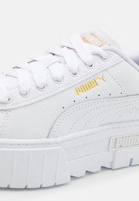 Sneaker bianco in pelle con suola piattaforma, caratterizzato da una finitura testurizzata, accento del logo dorato e lacci bianchi piatti.