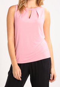 Blusa senza maniche rosa con davanti plissettato e scollatura a chiave; texture liscia e perline sottili lungo la scollatura. Pantaloni neri.