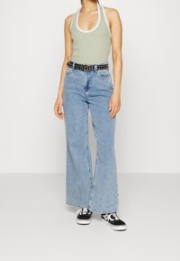 Světle zelený halter top s bílým lemem, spárovaný s vysokým pasem světle modrými širokými džínami a černými teniskami s bílými podrážkami a tkaničkami.