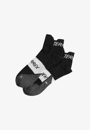 Chaussettes de sport noires avec le logo "TERREX" blanc, présentant un poignet côtelé, un orteil renforcé et un motif texturé au niveau de la semelle.