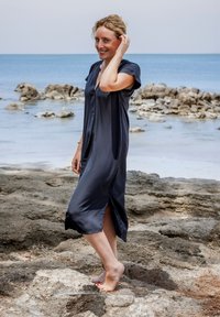 Navyblaues Satin-Kleid mit kurzen Ärmeln und V-Ausschnitt. Hat seitliche Schlitze und reicht bis zur Mitte der Waden. Wird barfuß an einem felsigen Strand getragen.