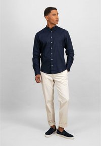 Camicia blu navy con colletto, abbinata a chinos color crema e scarpe slip-on scure. Tessuto liscio con dettaglio della tasca sul petto.
