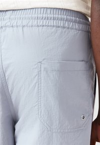 Pantaloni corti azzurri realizzati in un tessuto leggero e liscio, dotati di una cintura elastica, tasca posteriore e un piccolo dettaglio a occhiello.