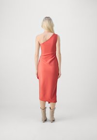 Robe corail asymétrique en tissu lisse, longueur midi avec une fente sur le côté, associée à des bottines beiges à la cheville avec un design western.