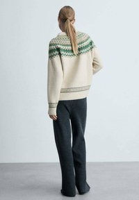 Kremeni vuneni pulover s zelenim geometrijskim uzorcima na jarmu i rukavima, uparen s tamnosivim pletenim širokim hlačama. Teksturirani finiš.