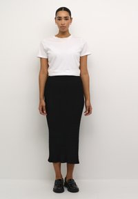 Jupe midi en tricot côtelé noire avec une silhouette ajustée, associée à un t-shirt blanc simple et des mocassins noirs. Design simple et élégant.