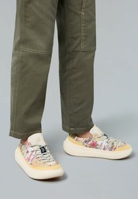 Baskets à motif floral avec une palette de couleurs beige et jaune. Semelle blanche épaisse, lacets gris et détail de logo sur la languette.