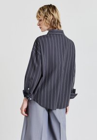 Blausa a righe grigio scuro con maniche lunghe, polsini con bottoni e colletto classico. Tessuto morbido e vestibilità rilassata.