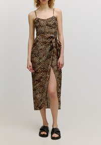 Leopardenmuster Midi-Kleid mit dünnen Trägern, seitlichem Schlitz und Knotendetail an der Taille; aus leichtem Stoff gefertigt; getragen mit schwarzen Sandalen.
