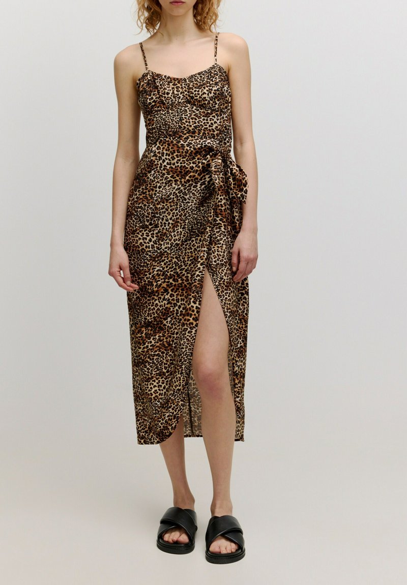 Leopardenmuster Midi-Kleid mit dünnen Trägern, seitlichem Schlitz und Knotendetail an der Taille; aus leichtem Stoff gefertigt; getragen mit schwarzen Sandalen.