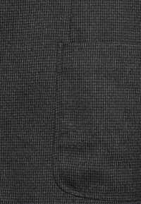 Tela gris con un patrón texturizado y un brillo sutil. Contiene un detalle de bolsillo. El material parece suave con finas líneas tejidas.