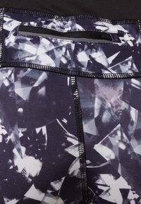 Schwarz-weiße Leggings mit geometrischem Muster, ausgestattet mit einem flachen Bund und einer kleinen mit Reißverschluss versehenen Tasche. Glattes, dehnbares Material.
