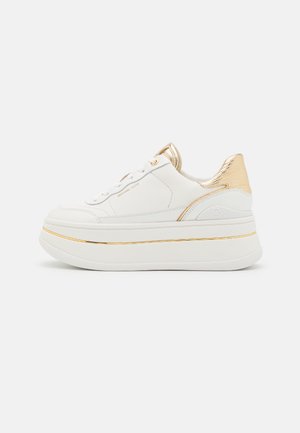 Baskets à plateforme blanches avec détails dorés sur le talon, la languette et le bord de la semelle, portant la marque "Michael Kors" sur le côté.