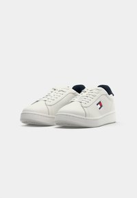 Pair of white low-top sneakers with white laces, thick soles, navy interior, and a red, white, and blue Tommy Hilfiger logo on the side.