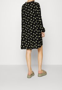 Musta pitkähihaista mekkoa vihreillä pilkuilla, polvimittainen, pehmeää kangasta, pyöreä kaula-aukko ja väljää istuvuutta. Yhdistetty oliivinvihreisiin sandaaleihin.