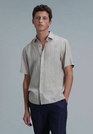Kurze Ärmel, hellbeige Leinenhemd mit Knopfverschluss, feiner Struktur und lockerer Passform, kombiniert mit marineblauen gestreiften Hosen.