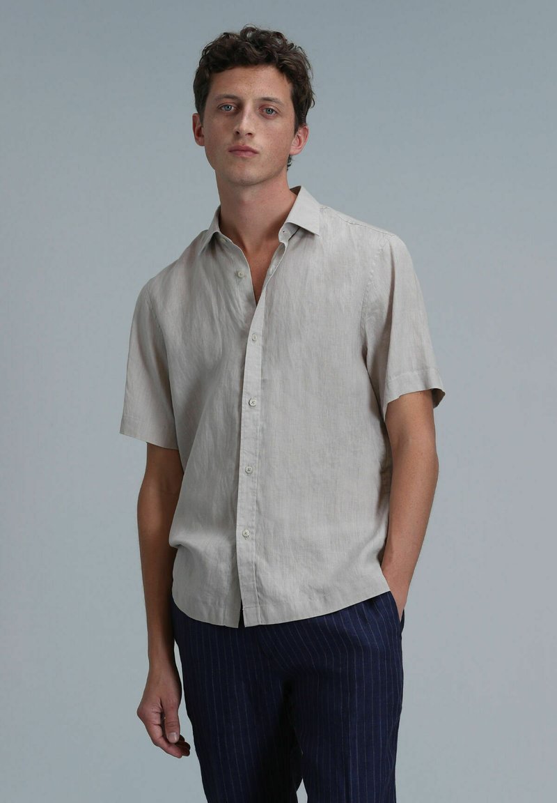 Korte mouwen, lichtbeige linnen shirt met een knoopsluiting, subtiele textuur en een relaxte pasvorm, gecombineerd met marineblauwe pinstriped broek.