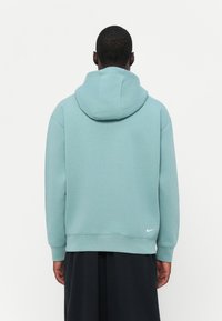 Fleece azul-turquesa com capuz, feito de material macio. Apresenta punhos e bainha canelados, com um pequeno logotipo branco da Nike na parte inferior direita.